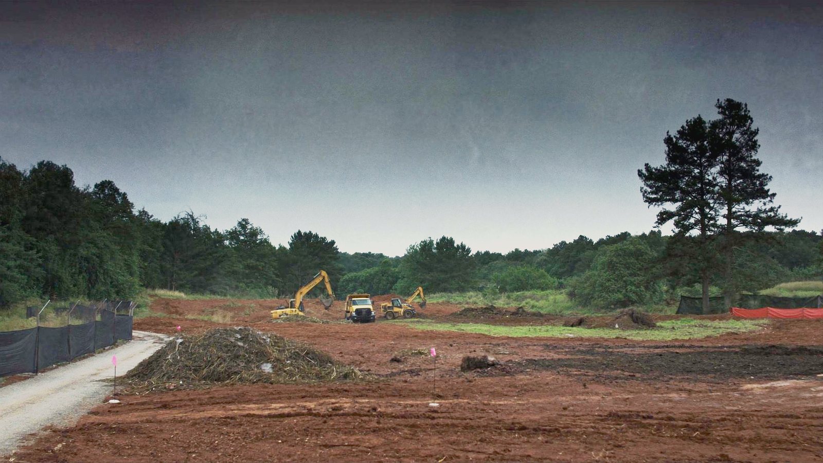 The same lot cleared and being graded, red earth, an excavator and a dozer at work